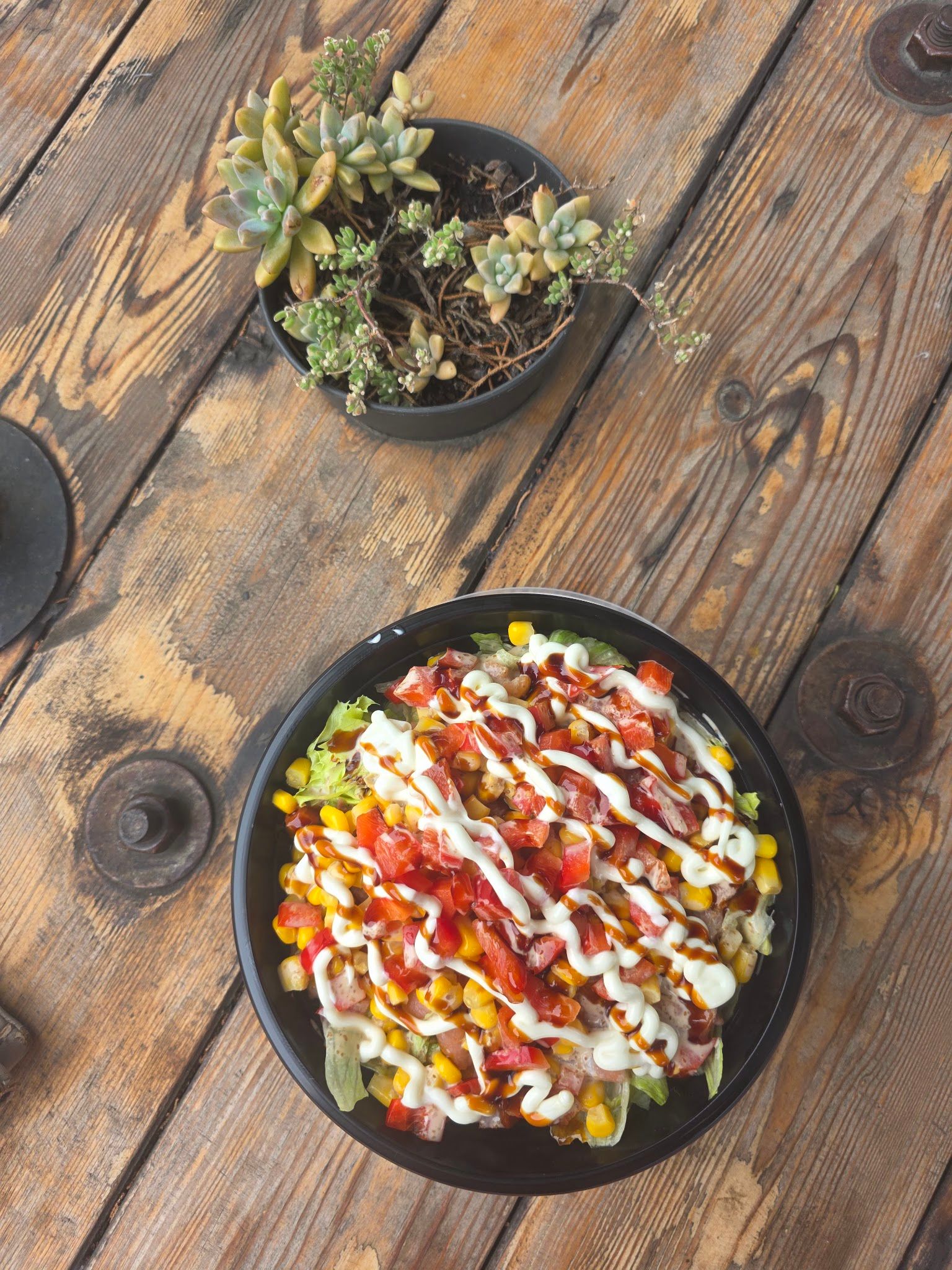 Overhead view of a sushi rice bowl with corn, tomato, lettuce and sauce drizzle on a wooden table